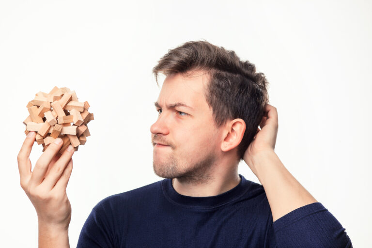 Attractive 25 year old business man looking confused and surprised at wooden puzzle on white studio background.